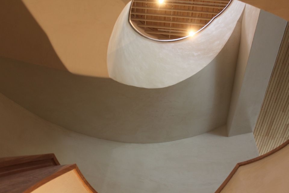 Blick eine geschwungene Treppe hinauf zu einem runden Oberlicht mit warmem Licht.