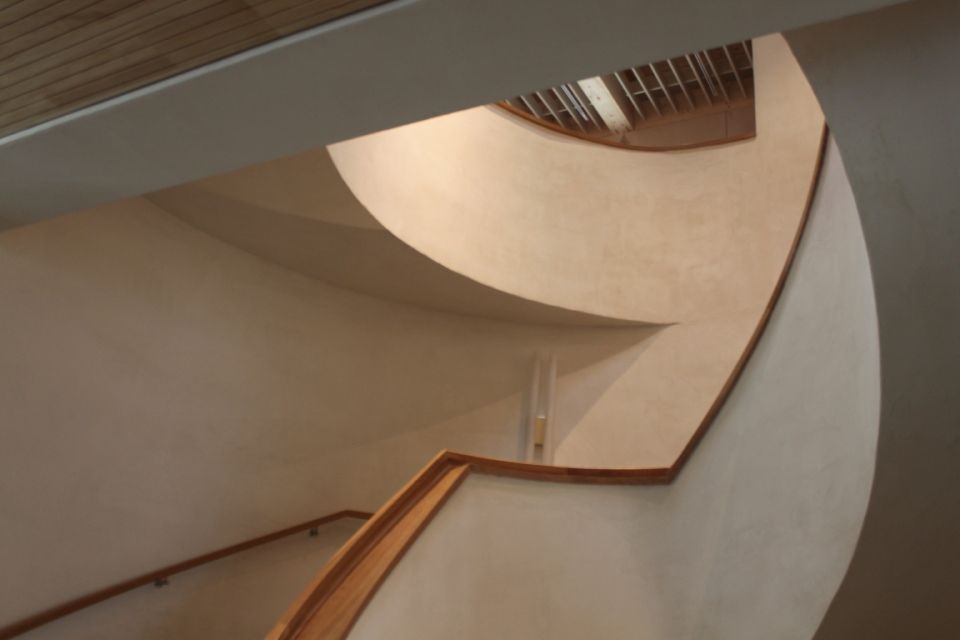 Geschwungene Treppe mit hölzernem Handlauf, die nach oben zu einer Lichtquelle führt.