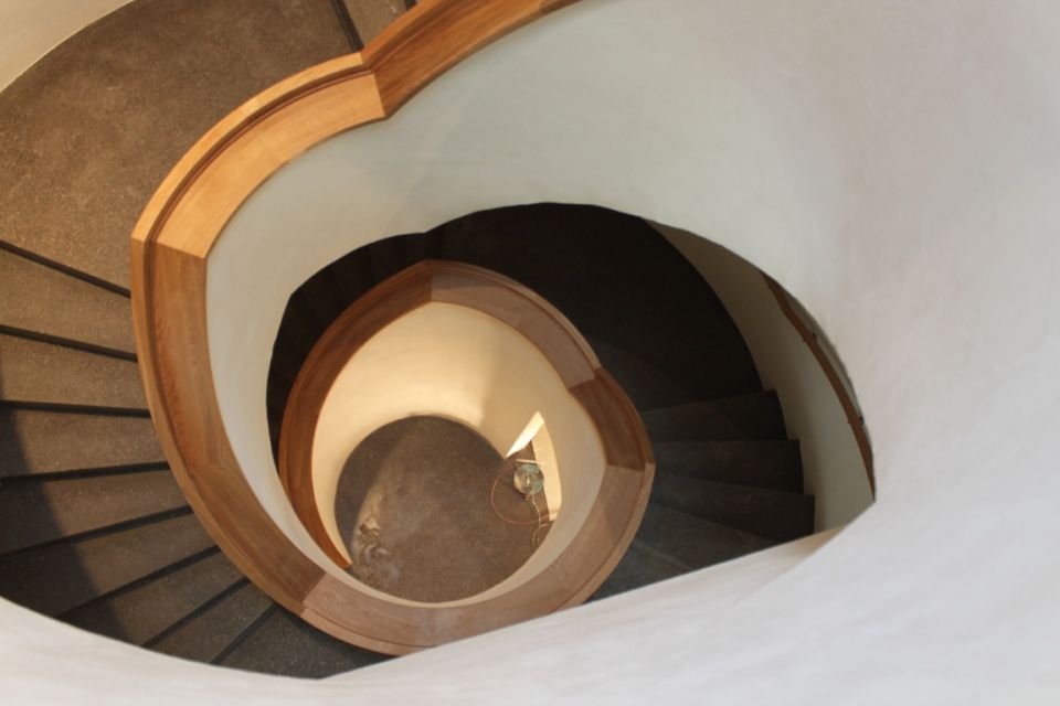 Wendeltreppe von oben, helles Holzgeländer, dunkelgraue Stufen, weisse Wände.