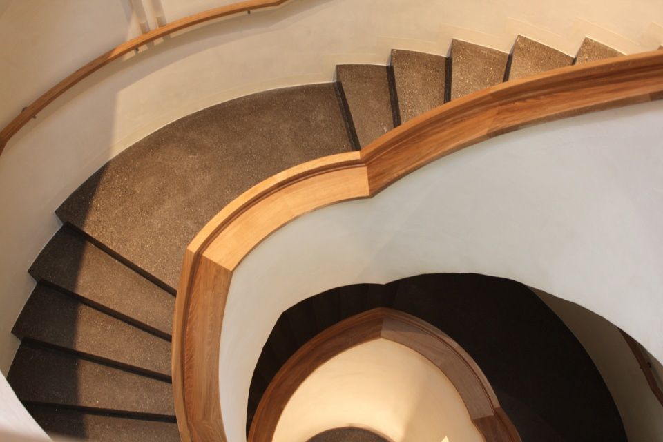 Wendeltreppe mit braunen Teppichstufen, hölzernem Handlauf und weissen Wänden.