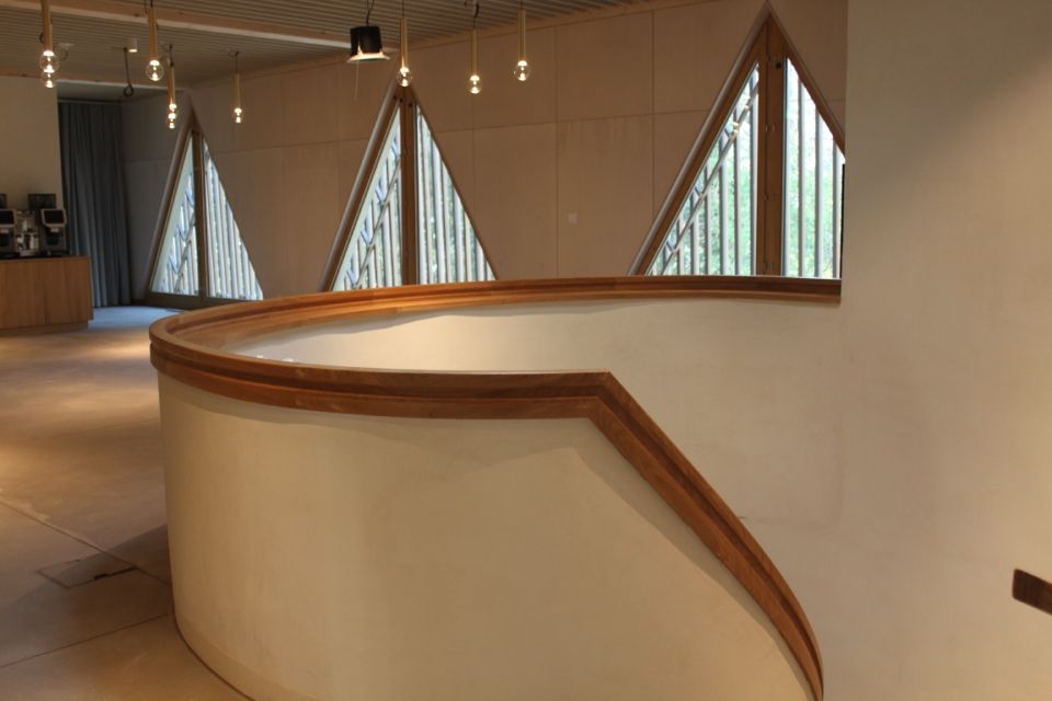 Weisse, geschwungene Wand mit Holzgeländer, dreieckigen Fenstern und Hängelampen in einem modernen Interieur.