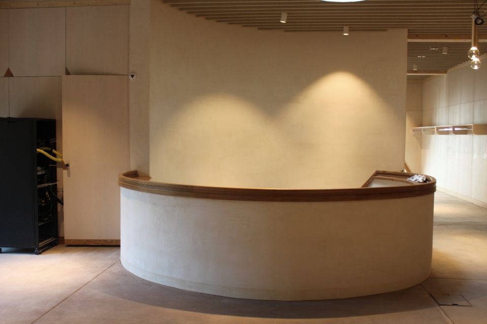 Geschwungener, weisser Empfangstresen mit Holzverkleidung. Leerer Raum mit Betonboden und Einbauleuchten.