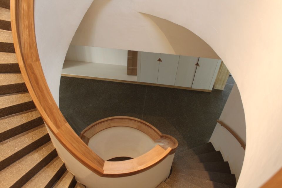 Eine geschwungene Holztreppe vor weissen Wänden. Blick von oben nach unten.