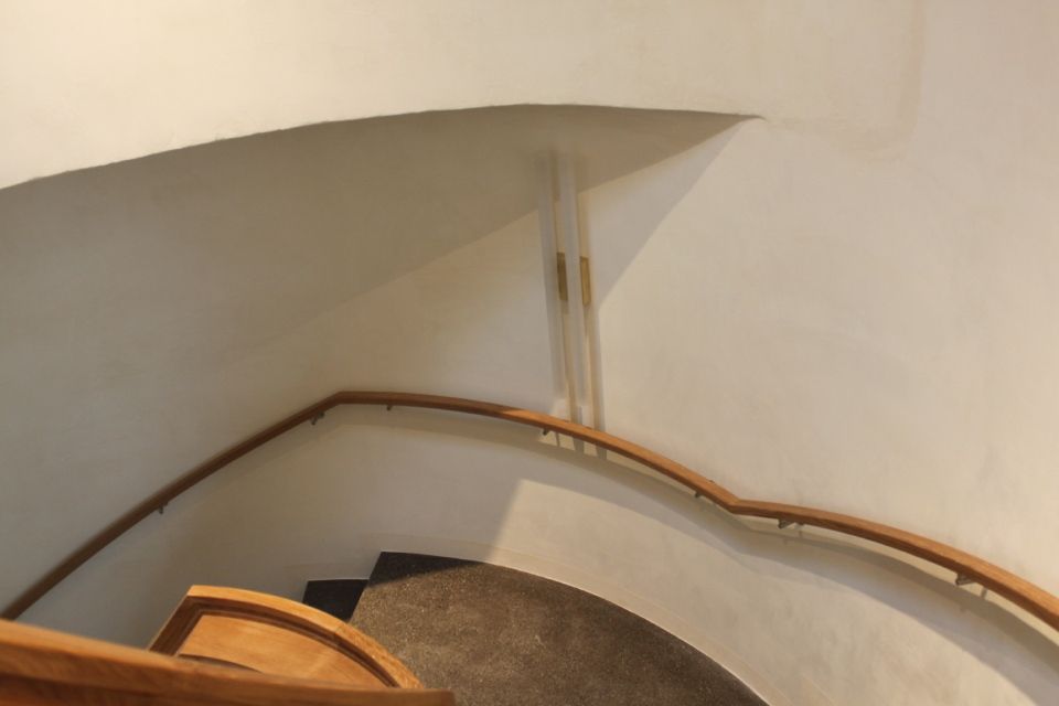 Blick von der Spitze einer geschwungenen Treppe mit hölzernem Handlauf vor weissen Wänden.