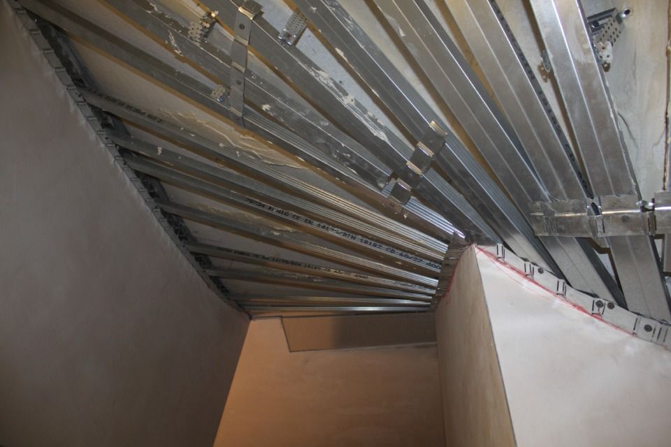 Metallrahmenkonstruktion und Gipskartondeckenkonstruktion in einem dreieckigen Raum mit verputzten Wänden.