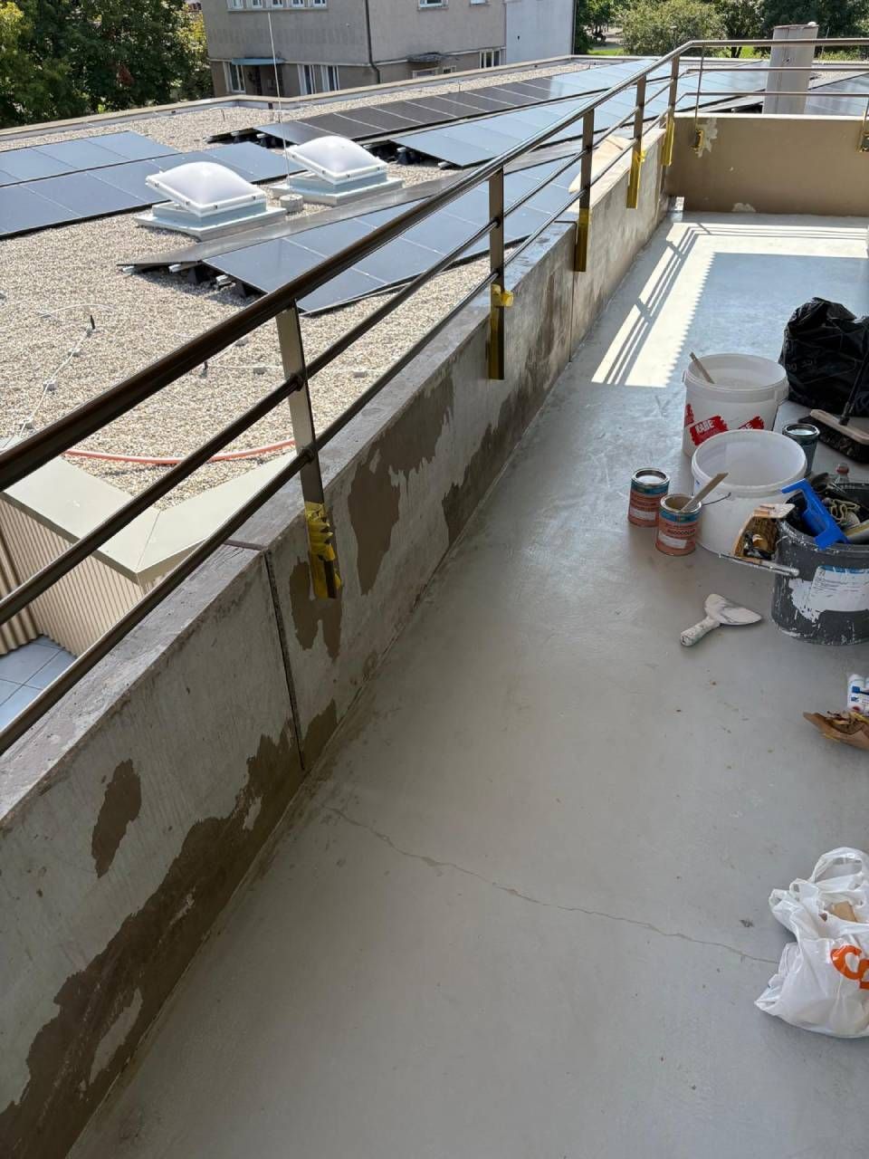 Dachterrasse mit Geländer, Solarpaneelen und Baumaterialien wie Eimern und Farbdosen.