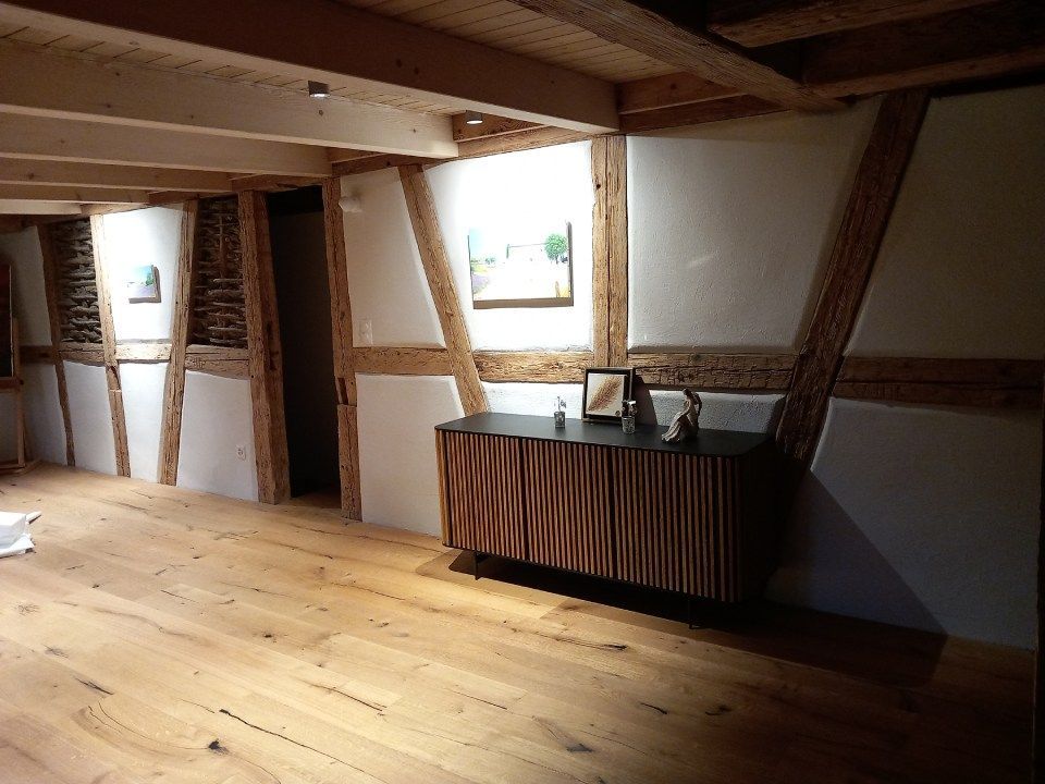 Innenansicht eines Zimmers mit freiliegenden Holzbalken, weissen Wänden, Holzboden und einem Holzschrank.