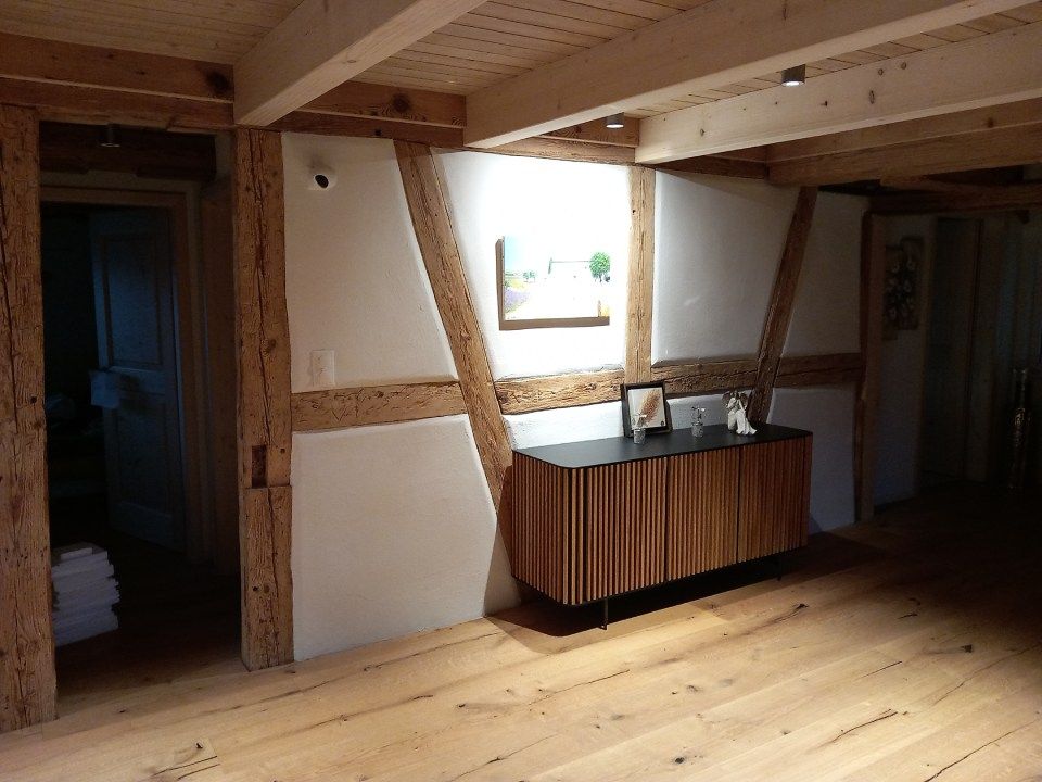 Der Innenraum besticht durch Holzbalken, einen hellen Holzboden und einen hellen Holzschrank. Weisse Paneele füllen die Zwischenräume der Balken.