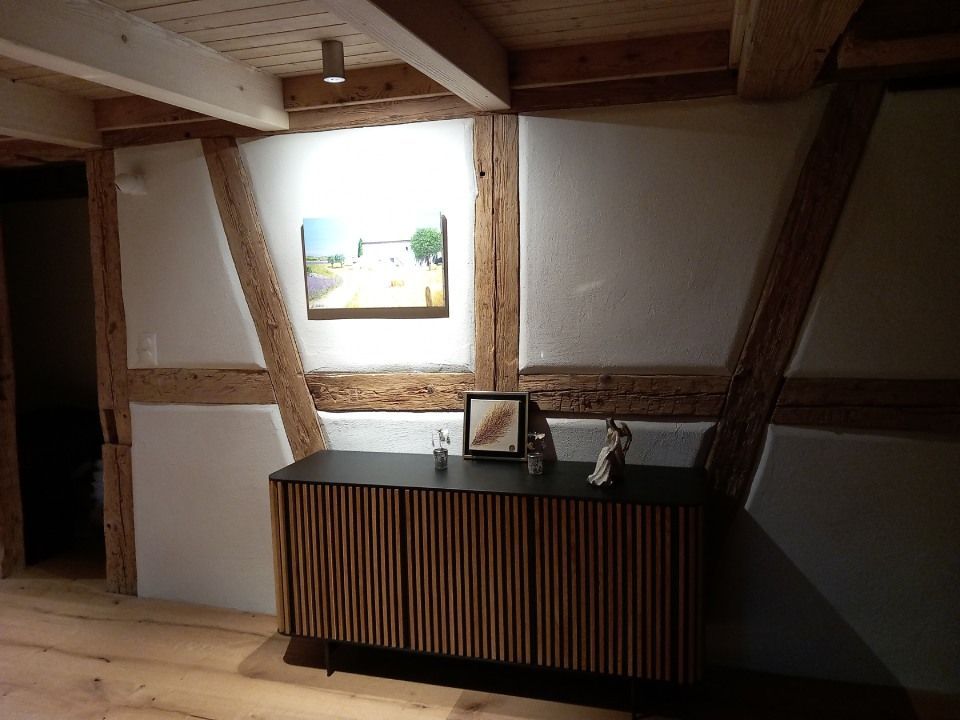Ein Holzschrank mit Verzierungen unterhalb eines Gemäldes an einer Wand mit sichtbaren Holzbalken.