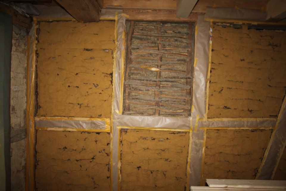 Innenwand mit freiliegendem Lehmmaterial und Holzrahmen.