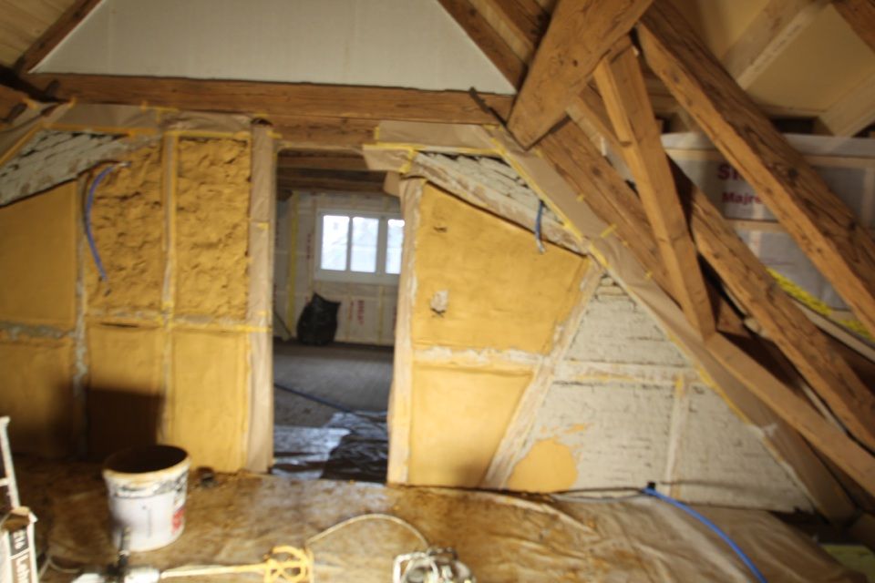 Dachboden im Umbau; sichtbare Dämmung, Holzbalken, Türöffnung zu einem Fenster.