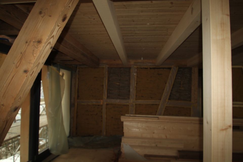 Innenansicht eines Dachbodens mit Holzbalken, Dämmung und einer teilweise errichteten Holzkonstruktion.