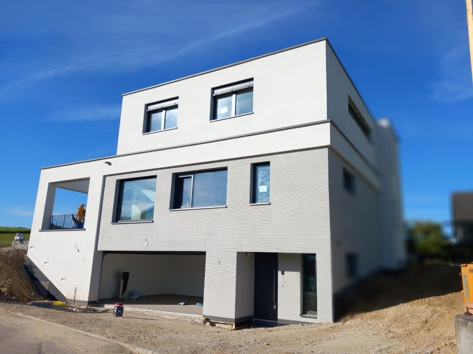 Modernes zweistöckiges Haus mit grau-weisser Fassade. Mit Garage und Fenstern mit Blick auf den blauen Himmel.