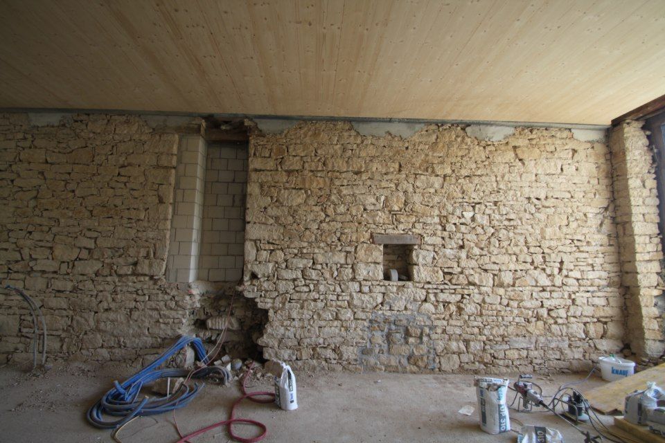 Innenansicht einer im Bau befindlichen Steinmauer mit freiliegender Decke und Baumaterialien.