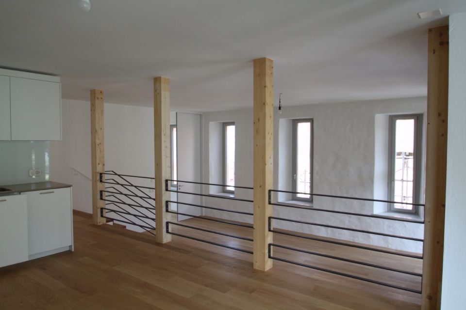 Innenansicht eines modernen Lofts mit Holzböden, weissen Wänden und schwarzem Geländer.