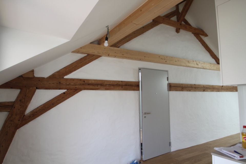 Interieur mit freiliegenden Holzbalken, weissen Wänden und einer grauen Tür.