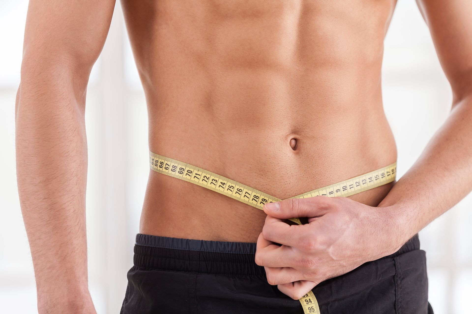 El hombre mide su cintura con una cinta métrica amarilla, mostrando unos abdominales tonificados.