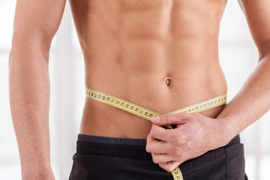 El hombre mide su cintura con una cinta métrica amarilla, mostrando unos abdominales tonificados.