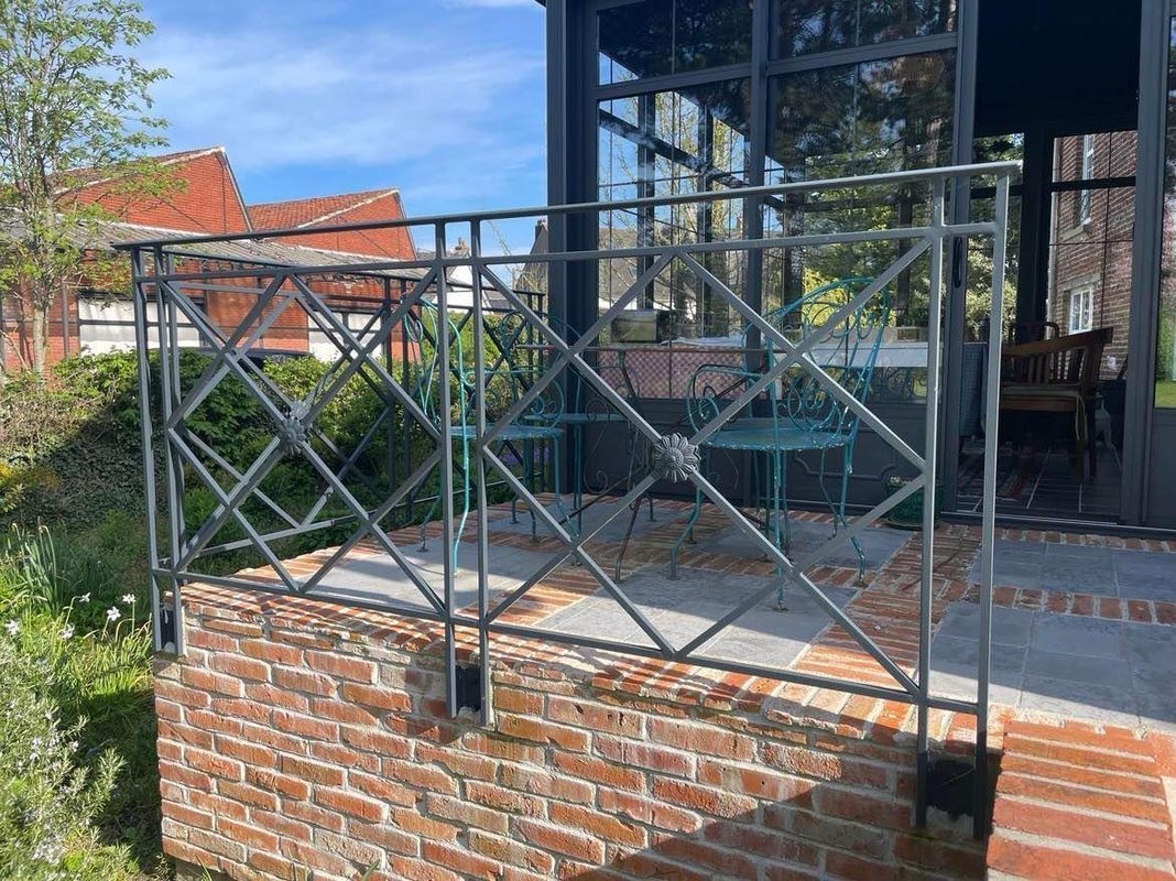Porche en briques avec rambarde en métal noir devant une maison à façade vitrée par une journée ensoleillée