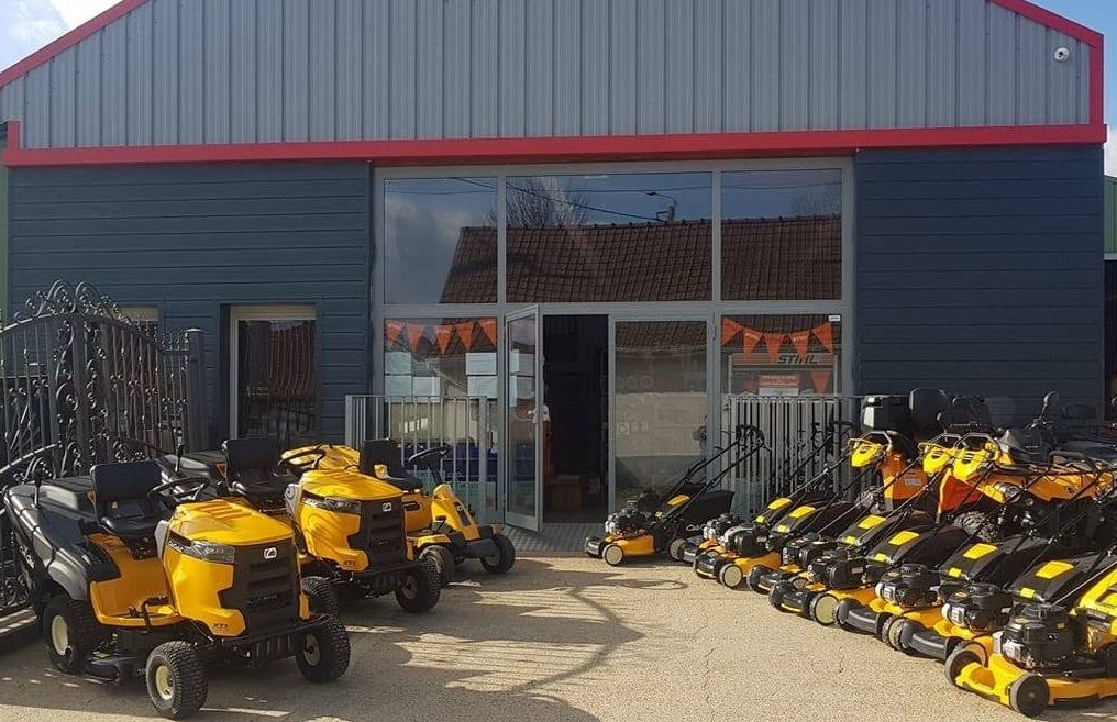 Tondeuse à gazon autoportée jaune, stationnée dans une allée près de maisons.