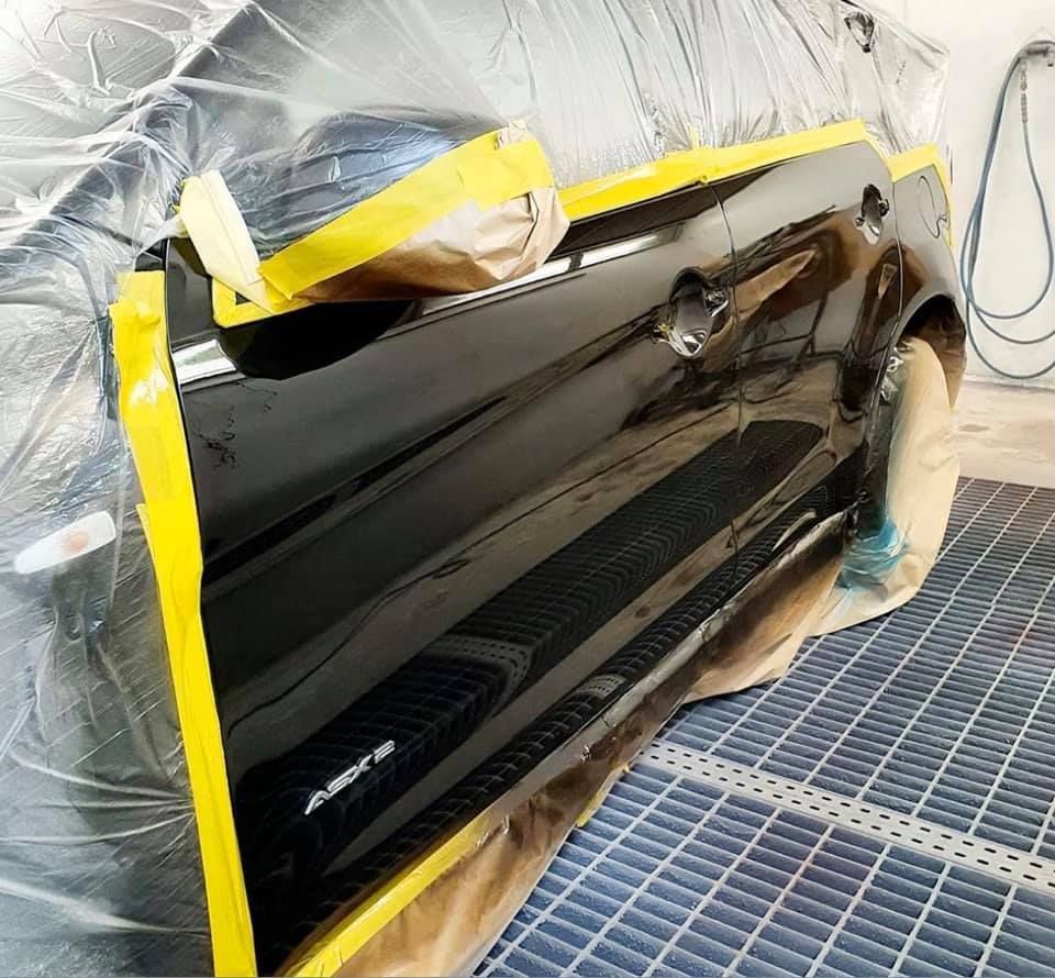 Puerta de un automóvil negro que se está pintando y protegiendo con cinta adhesiva amarilla en una cabina de pintura.