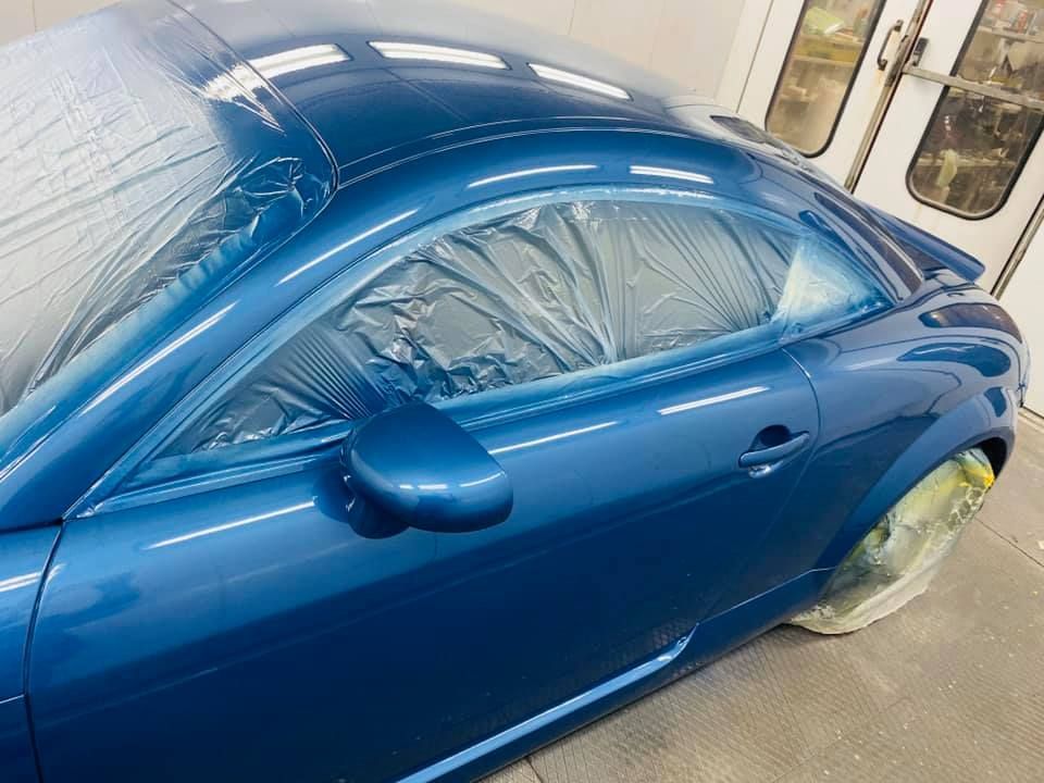 Coche azul en cabina de pintura, ventanas y ruedas cubiertas, mostrando un acabado brillante recién pintado.