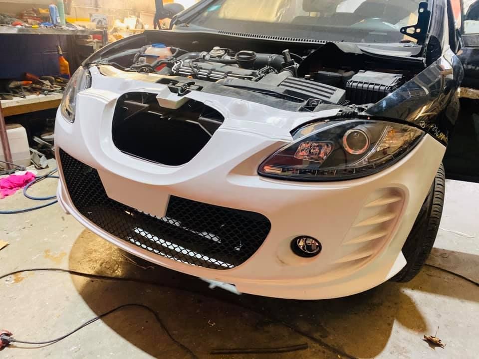 Automóvil blanco con el capó abierto, mostrando el motor; parachoques delantero en proceso de reparación.