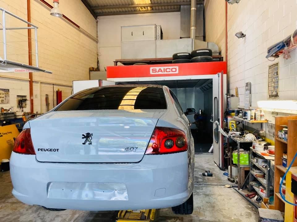 Peugeot 407 blanco en un taller de carrocería, parcialmente pintado. Cabina de pintura GAICO visible al fondo.
