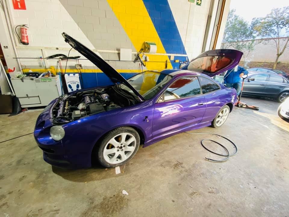 Coche morado en taller con el capó y el maletero abiertos, en proceso de reparación.