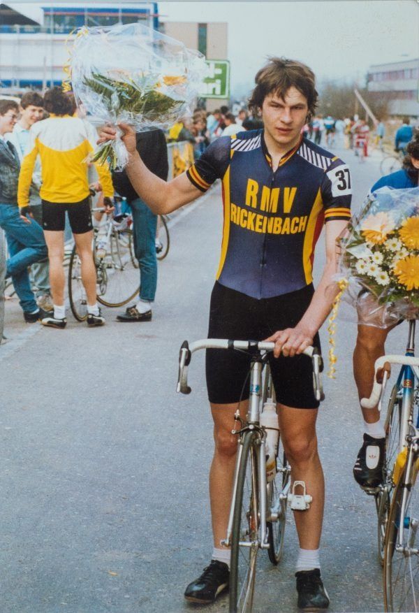 Radfahrer im schwarz-gelben RMV-Wackerhausen-Trikot steht nach einem Rennen mit seinem Fahrrad neben sich und hält einen Pokal in der Hand.