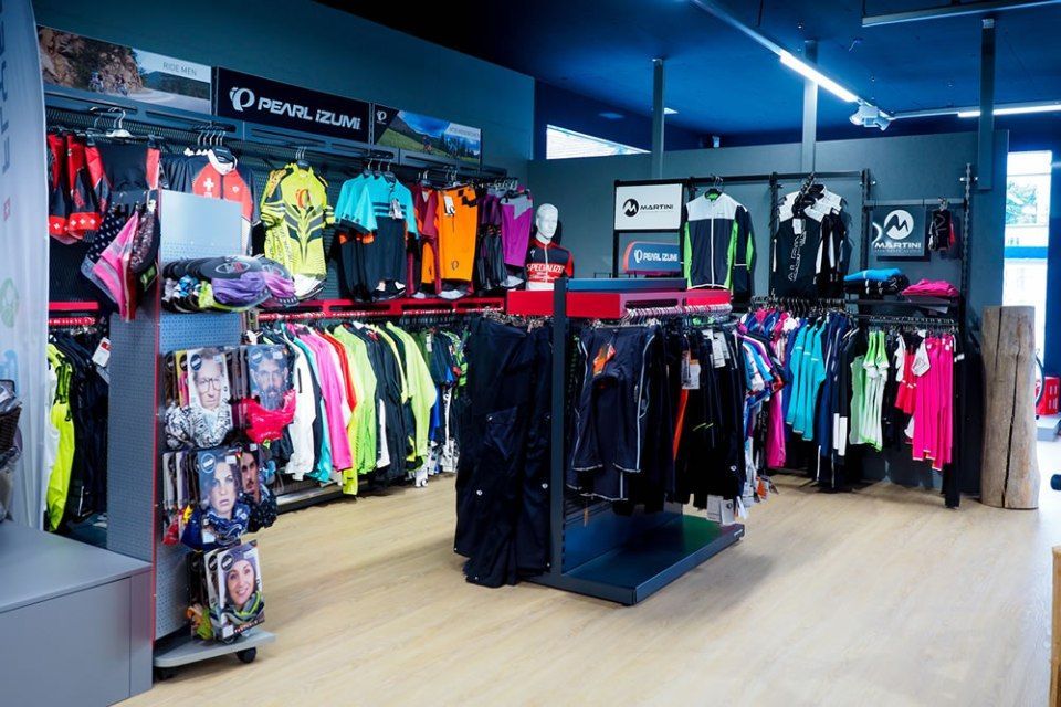Innenansicht eines Bekleidungsgeschäfts mit Regalen voller bunter Jacken, Hemden und Sportbekleidung unter hellem Licht