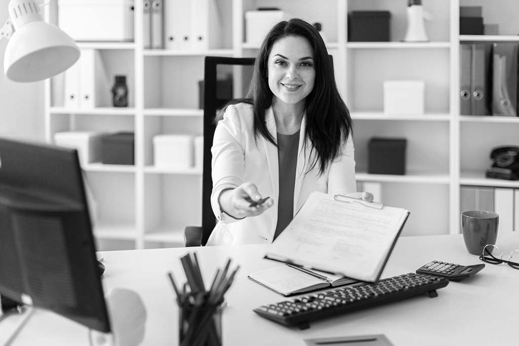 Une femme assise à un bureau, elle tend un stylo et une feuille