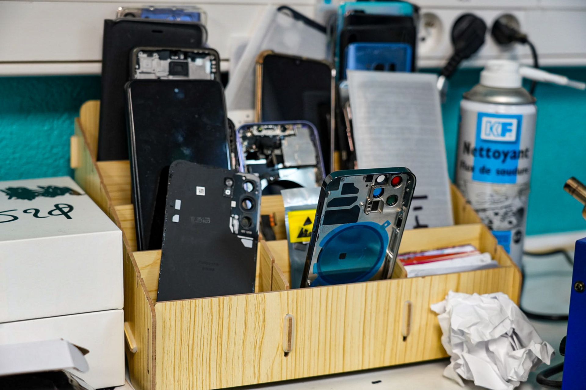 Atelier de réparation de téléphones portables avec téléphones démontés et composants dans un organisateur en bois.
