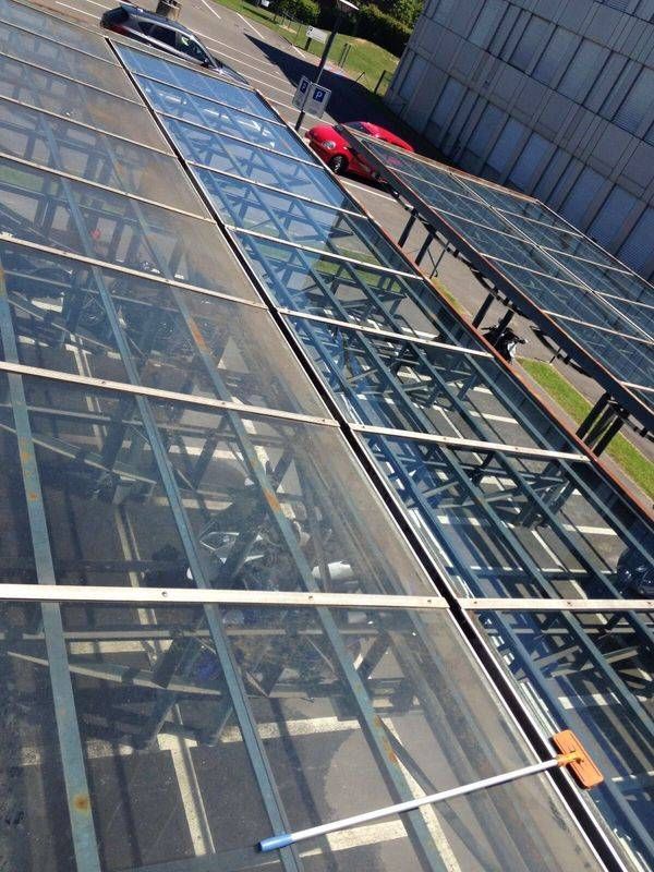 Passerelle vitrée sous une voiture rouge, avec des structures en acier et des panneaux inclinés.