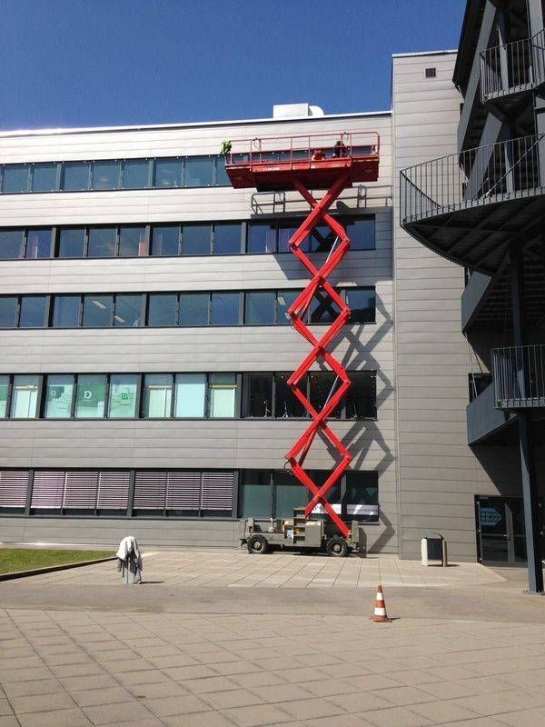 Une nacelle élévatrice rouge atteint le sommet de la façade d'un immeuble de plusieurs étages.