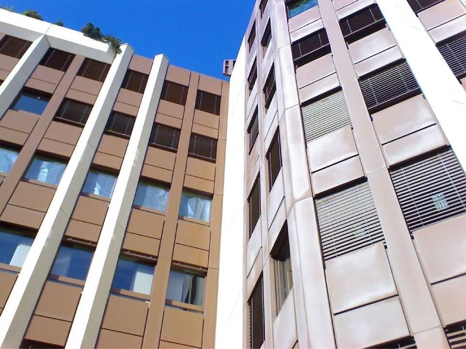Vue en contre-plongée d'immeubles d'appartements modernes aux façades beiges et blanches se détachant sur un ciel bleu.