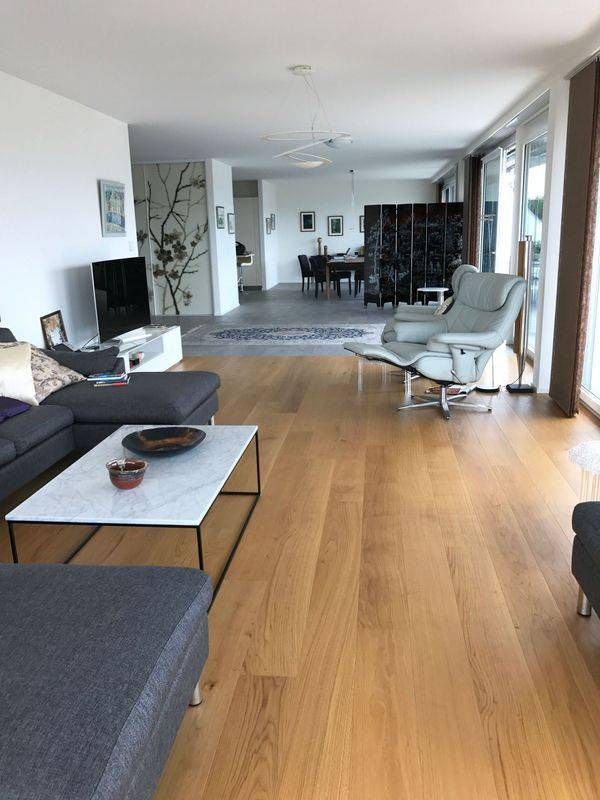 Salon moderne avec canapé gris, table basse blanche, parquet et grandes fenêtres