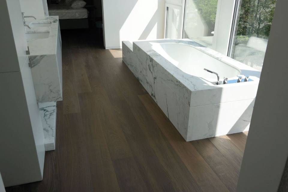 Pièce moderne et lumineuse avec parquet, placards blancs intégrés et une grande banquette près de la fenêtre.
