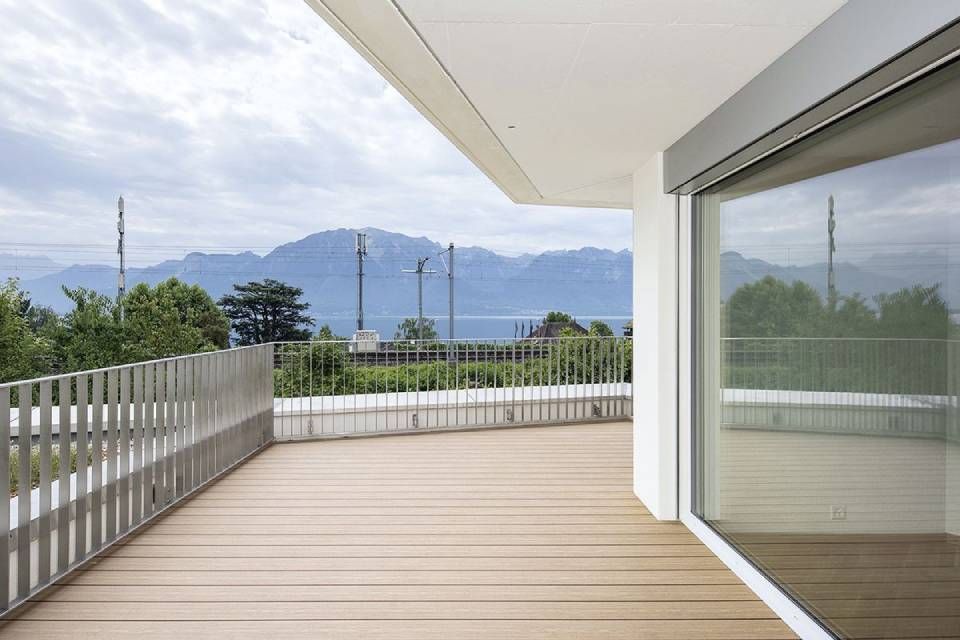 Balcon-terrasse moderne avec portes vitrées, rambarde blanche et vue sur la montagne sous un ciel nuageux