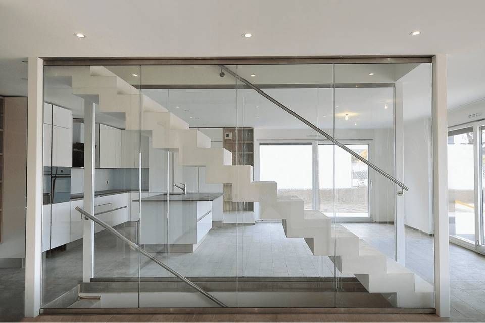 Intérieur moderne à aire ouverte avec cloison vitrée, escalier suspendu et cuisine blanche lumineuse