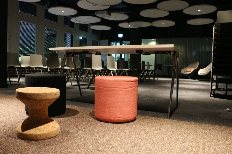 Salon de bureau moderne avec tabouret en bois, pouf corail et table de réunion sous des luminaires circulaires au plafond
