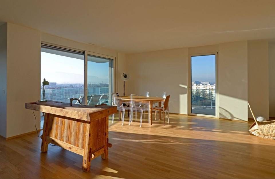 Appartement moderne et lumineux avec parquet, îlot central, table à manger et vue sur la ville à travers de grandes fenêtres.