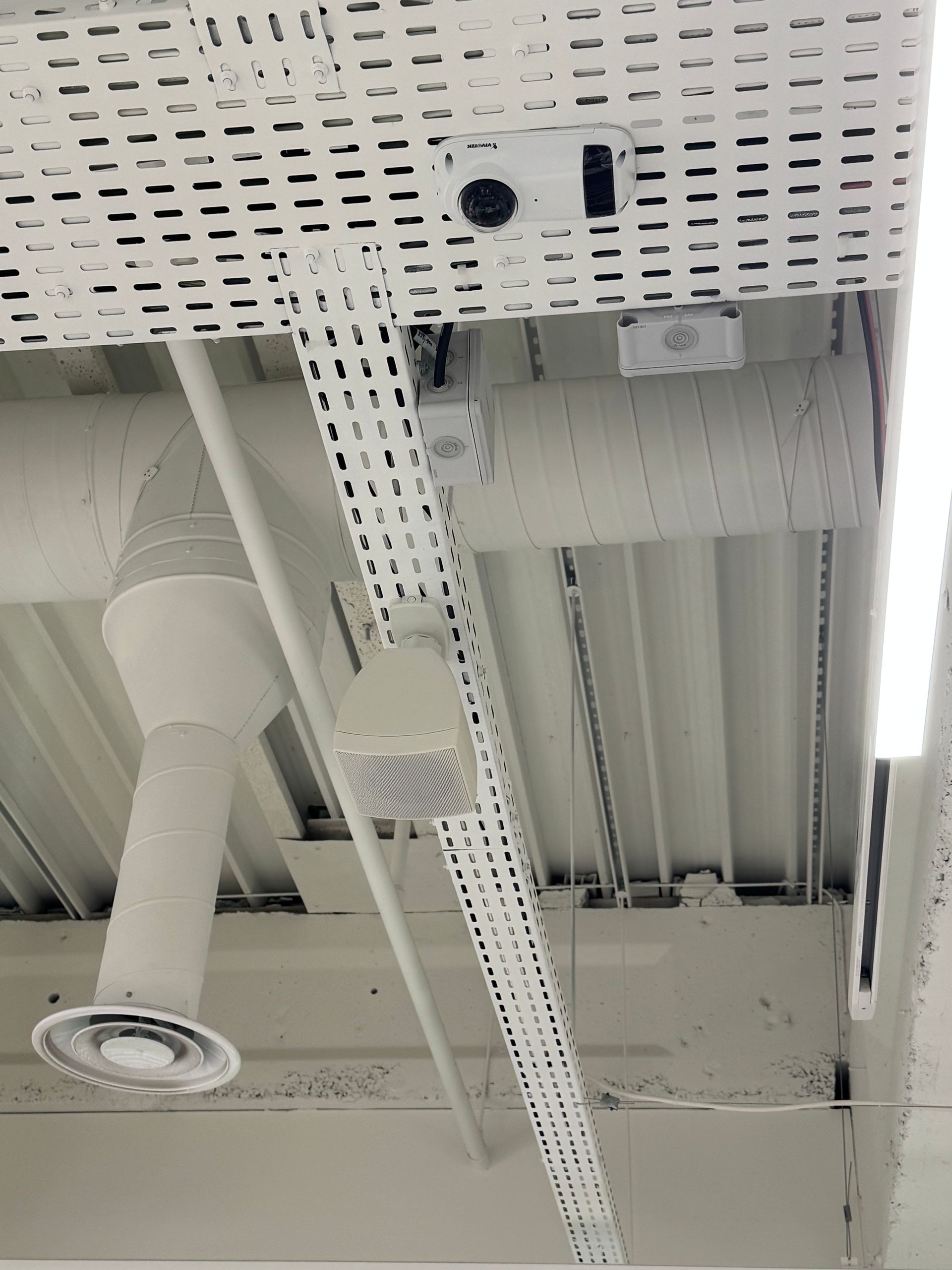Conduits, tuyaux, chemins de câbles et éclairages fluorescents blancs fixés au plafond dans un intérieur industriel.