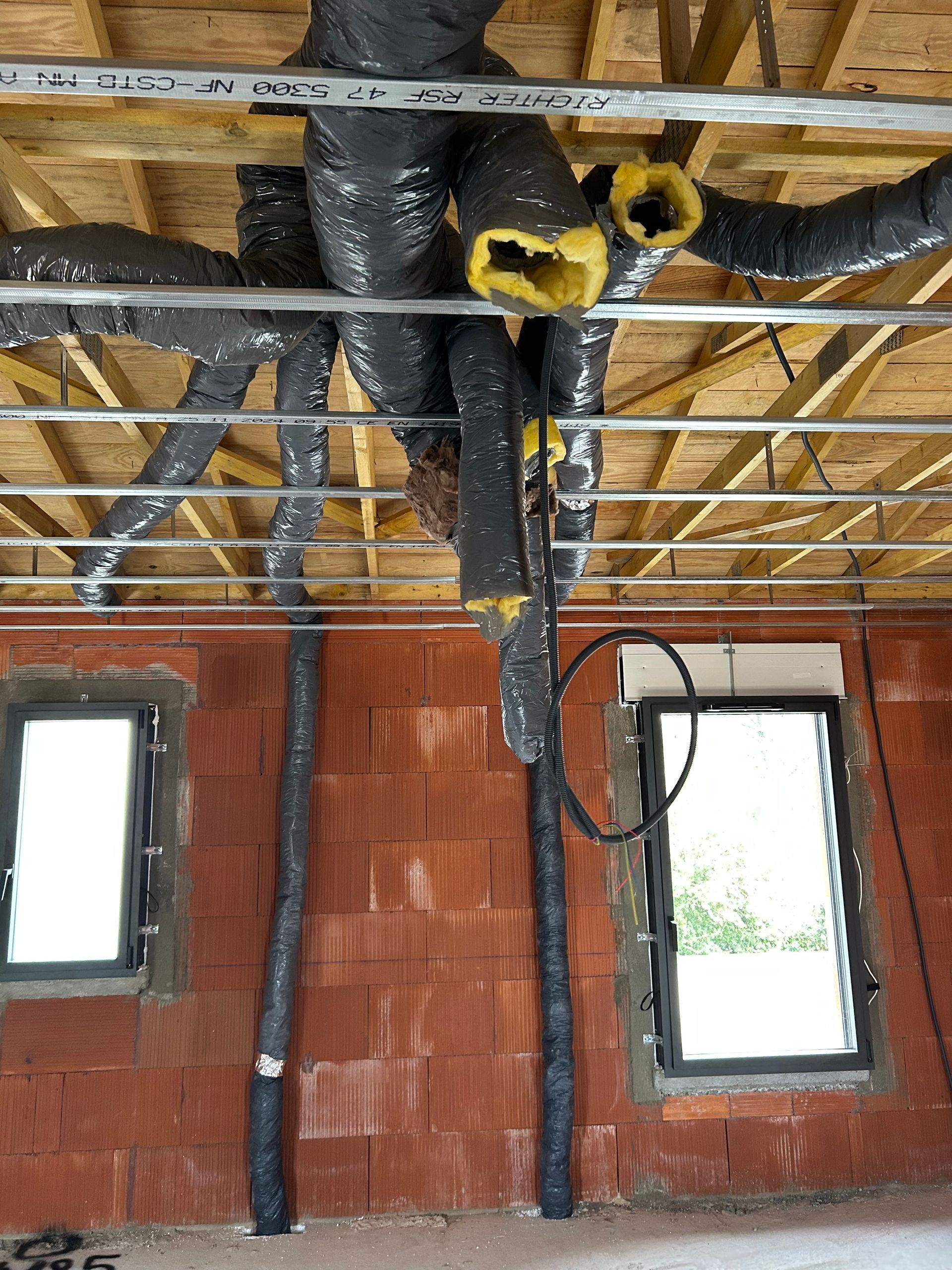 Conduits et câbles électriques isolés noirs apparents dans une pièce en briques non finie.