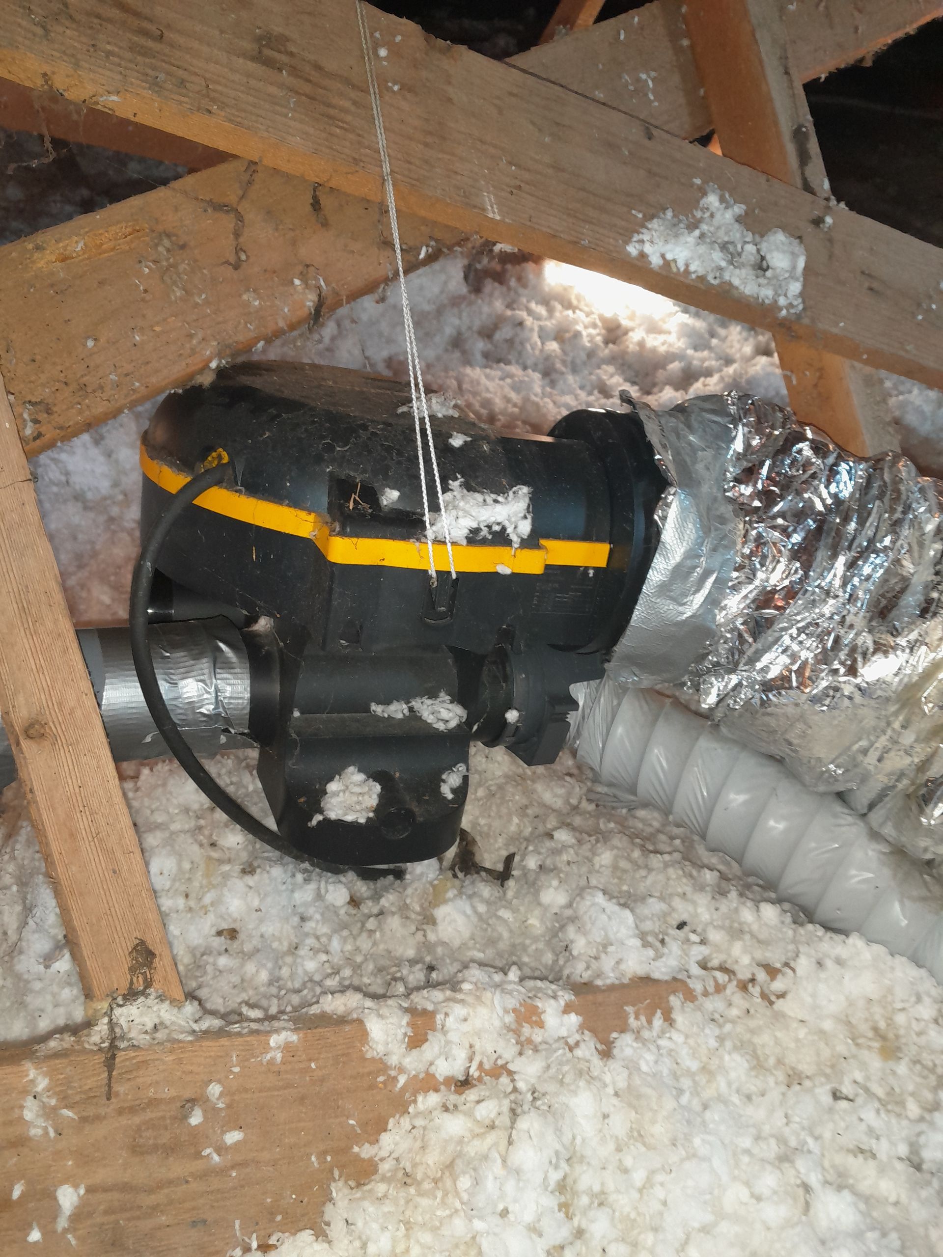 Moteur de ventilateur de climatisation noir avec une bande jaune, installé dans les chevrons du grenier.