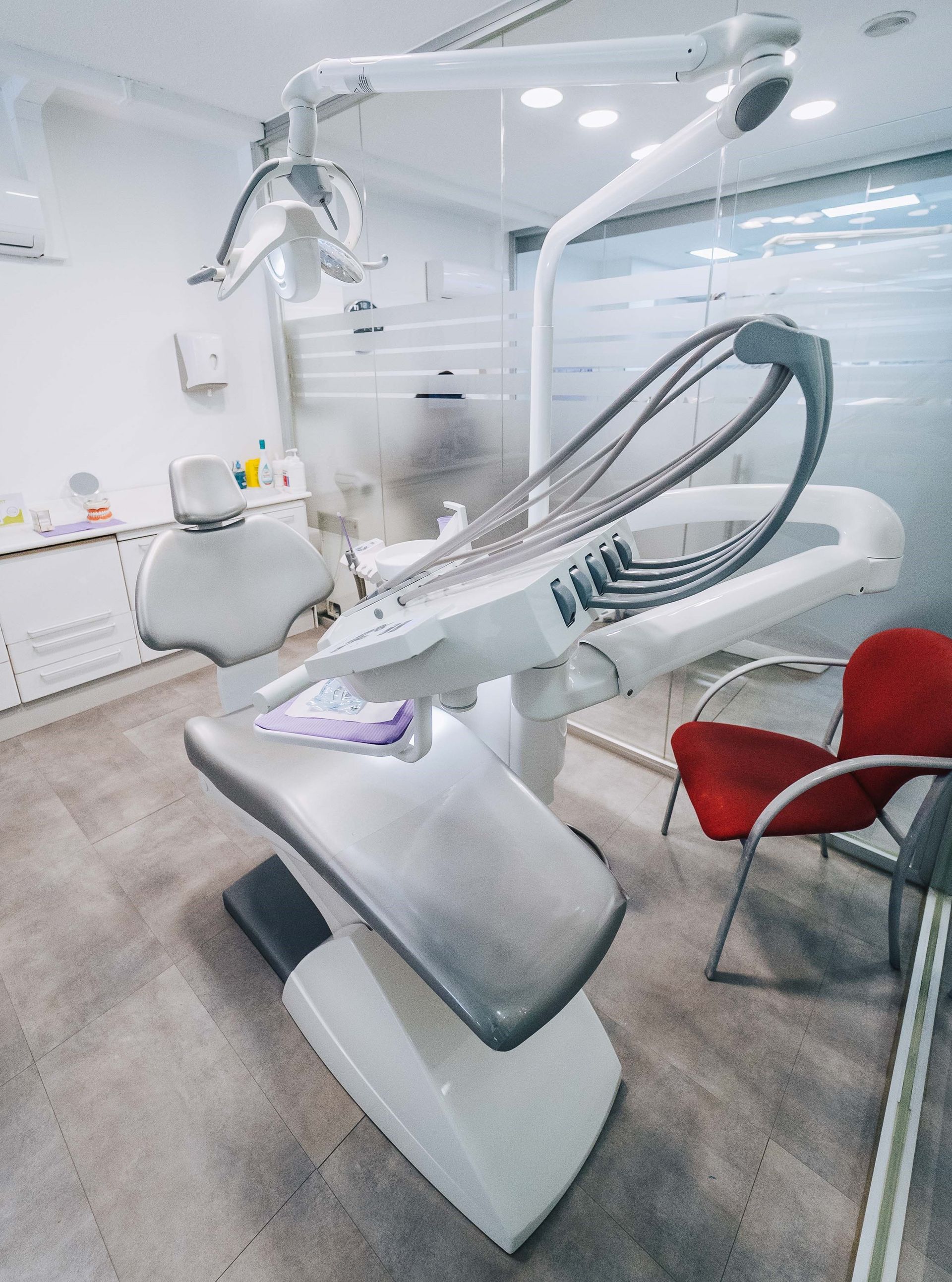 Un consultorio dental con un sillón dental y una silla roja.