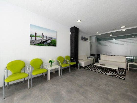 Una sala de espera con sillas verdes y un sofá blanco.