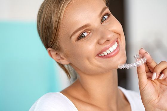Una mujer sonríe mientras sostiene un aparato transparente en sus dientes.