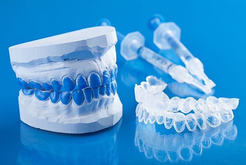 Un modelo de dientes y bandejas de blanqueamiento dental sobre una superficie azul.