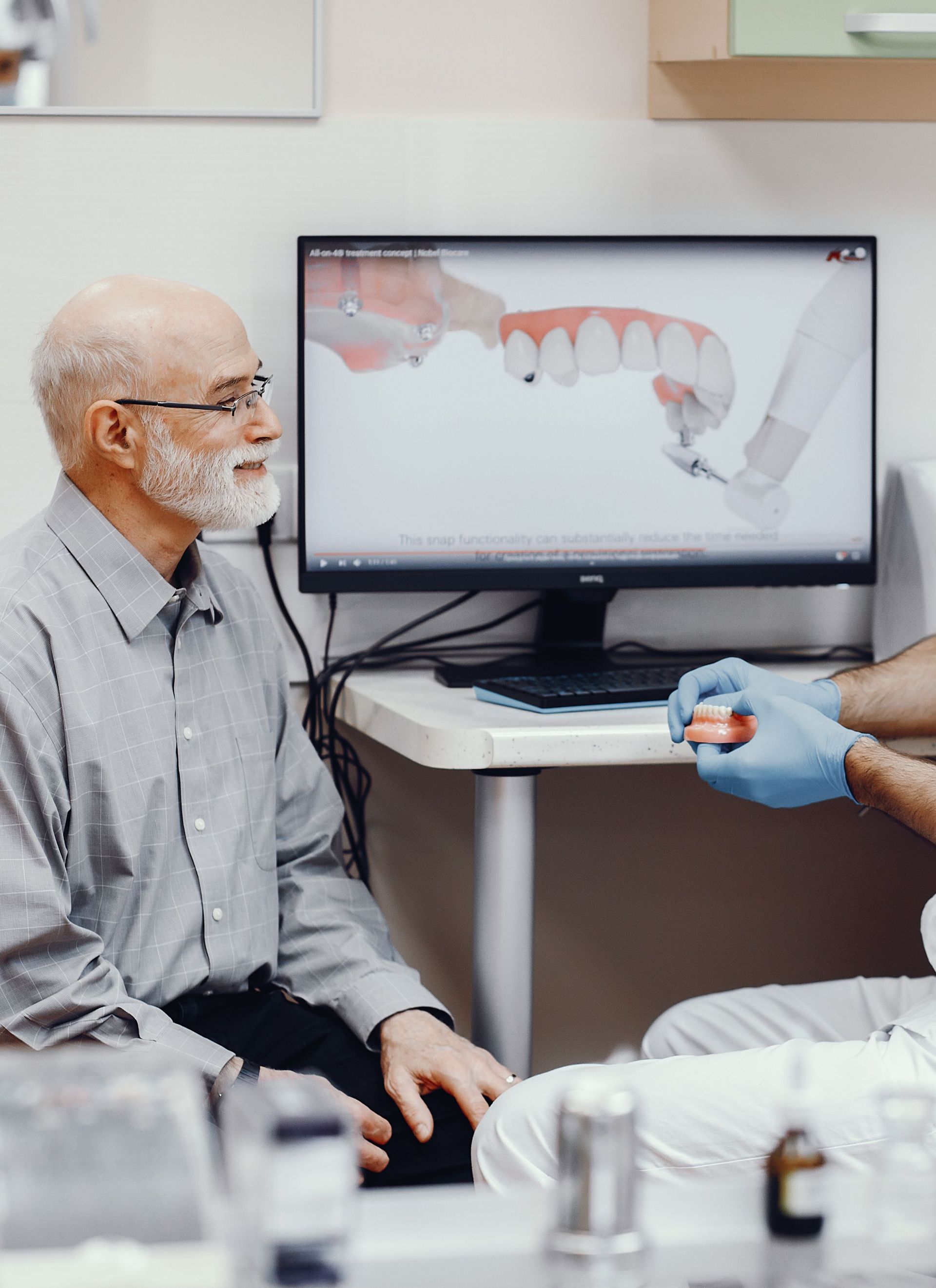 Un hombre mayor está sentado frente a una computadora hablando con un dentista.